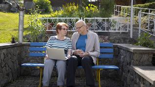 Zwei Senioren auf einer Bank mit Laptop auf dem Schoß (verweist auf: Im Alter gut leben auf dem Land – Unterstützungsangebote aufbauen und nutzen)