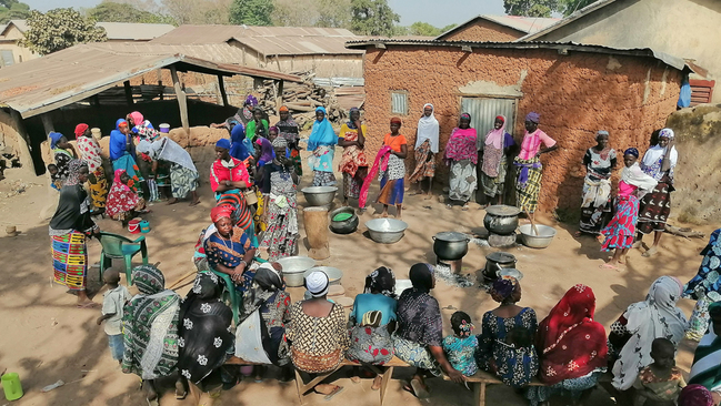 Viele Frauen sitzen auf Bänken in einem afrikanischen Dorf 