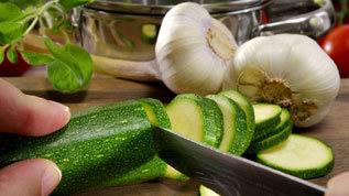 Hand mit Zucchini, die geschnitten wird