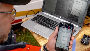 Mann mit Mobiltelefon vor einem Laptop Mann mit Mobiltelefon vor einem Laptop