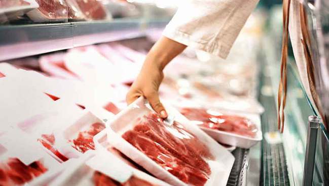 Eine Hand greift eine Packung mit Fleisch Eine Hand greift eine Packung mit Fleisch
