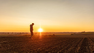Landwirt geht über ein gepflügtes Feld bei Sonnenuntergang Landwirt geht über ein gepflügtes Feld bei Sonnenuntergang