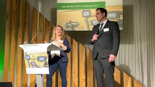 verweist auf: Videos der Konferenzvorträge - Kurzvorstellungen der Experimentierfelder Zwei Personen beim Vortrag auf einer Bühne (verweist auf: Videos der Konferenzvorträge - Kurzvorstellungen der Experimentierfelder)