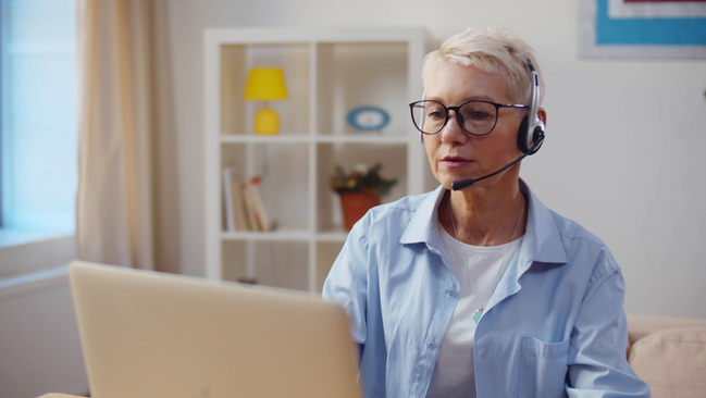 Eine Frau sitzt mit einem Head-Set vor einem Laptop.